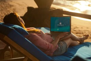 Minimalist remote work setup featuring a laptop on a wooden table with a stunning, bright view of a turquoise ocean and wh...