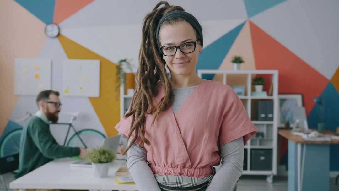 A professionally dressed and confident entrepreneur stands in a bright, modern office with large windows, representing the autonomy and success of a franchise owner.