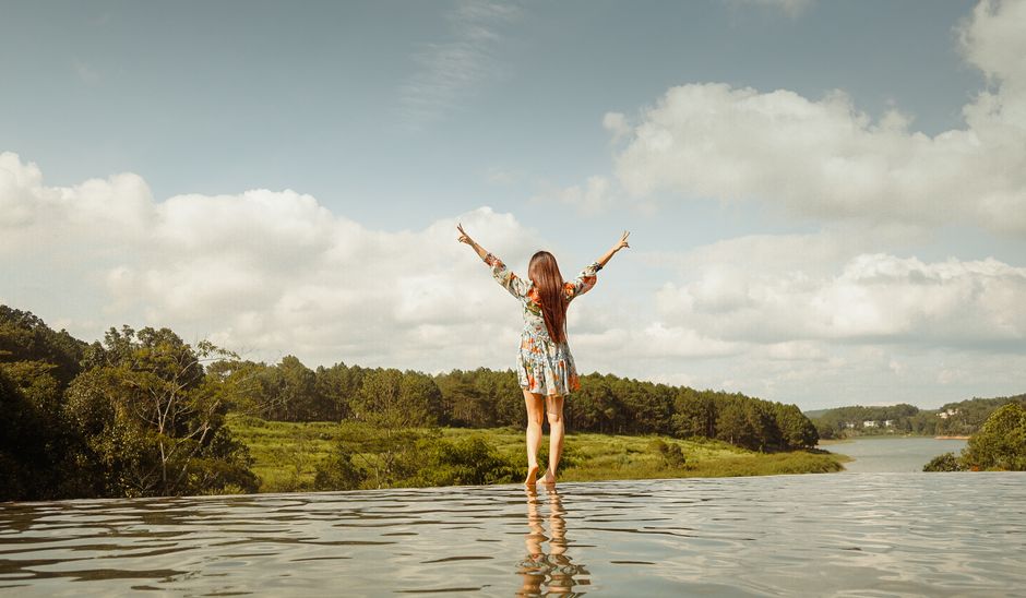 A woman relaxes by a luxurious infinity pool with a stunning ocean view, casually using her smartwatch, illustrating a seamless and tech-enabled holiday experience.